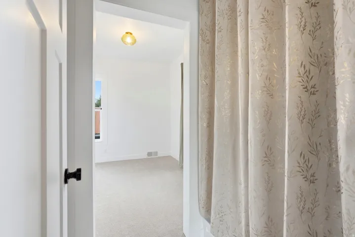 Room entry featuring a white paneled door with black hardware, leading to a space with light-toned carpet flooring, white walls, a single window, and a ceiling-mounted light fixture