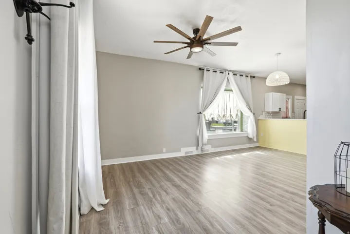 Spacious room featuring wood-finish flooring, a contemporary ceiling fan, and ample natural light from a window with white trim