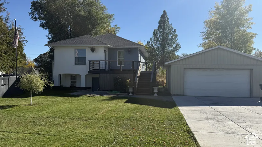 Two-story exterior with mixed siding, elevated wooden deck, attached stairs, concrete driveway, and detached garage