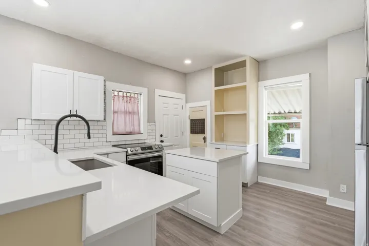 Open-concept kitchen featuring white shaker cabinetry, an island with countertop seating, stainless steel appliances, a subway tile backsplash, and light wood-finish flooring