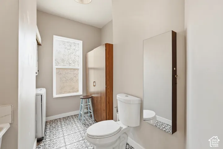 Bathroom featuring a patterned tile floor, a window with frosted glass, a white toilet, and a wall-mounted mirror