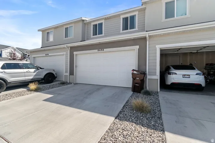 Contemporary facade featuring light gray siding and stucco, white-framed windows, two single-car garages, and concrete driveways with decorative rock landscaping