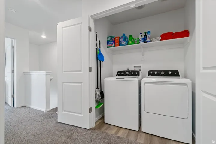 Dedicated laundry area featuring a white washer and dryer, wood-finish flooring, and a storage shelf