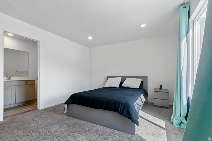 Carpeted sleeping area featuring recessed lighting, a sliding glass door with window treatments, and a private bathroom entrance