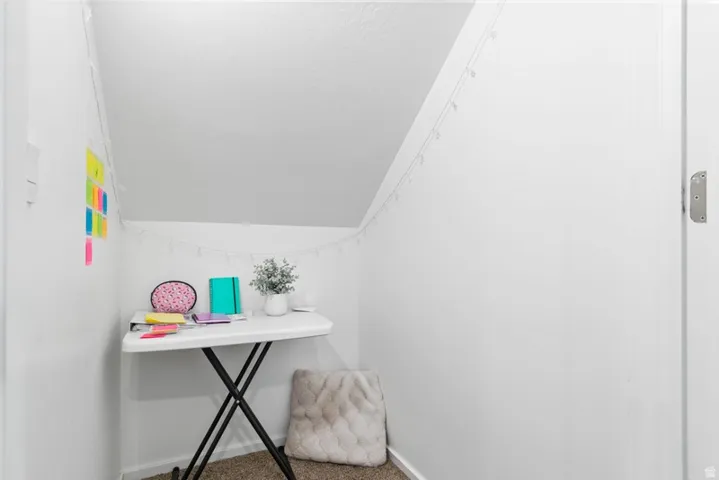 Sloped ceiling space featuring white painted walls and carpeted flooring