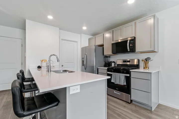 Modern kitchen featuring a spacious island with an integrated sink, light-toned countertops, contemporary cabinetry, stainless steel appliances, and wood-finish flooring