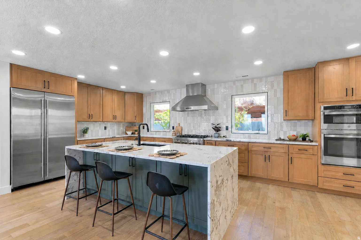 Expansive kitchen featuring a large island with seating, stainless steel appliances, light wood-finish cabinetry, a patterned tile backsplash, and recessed lighting