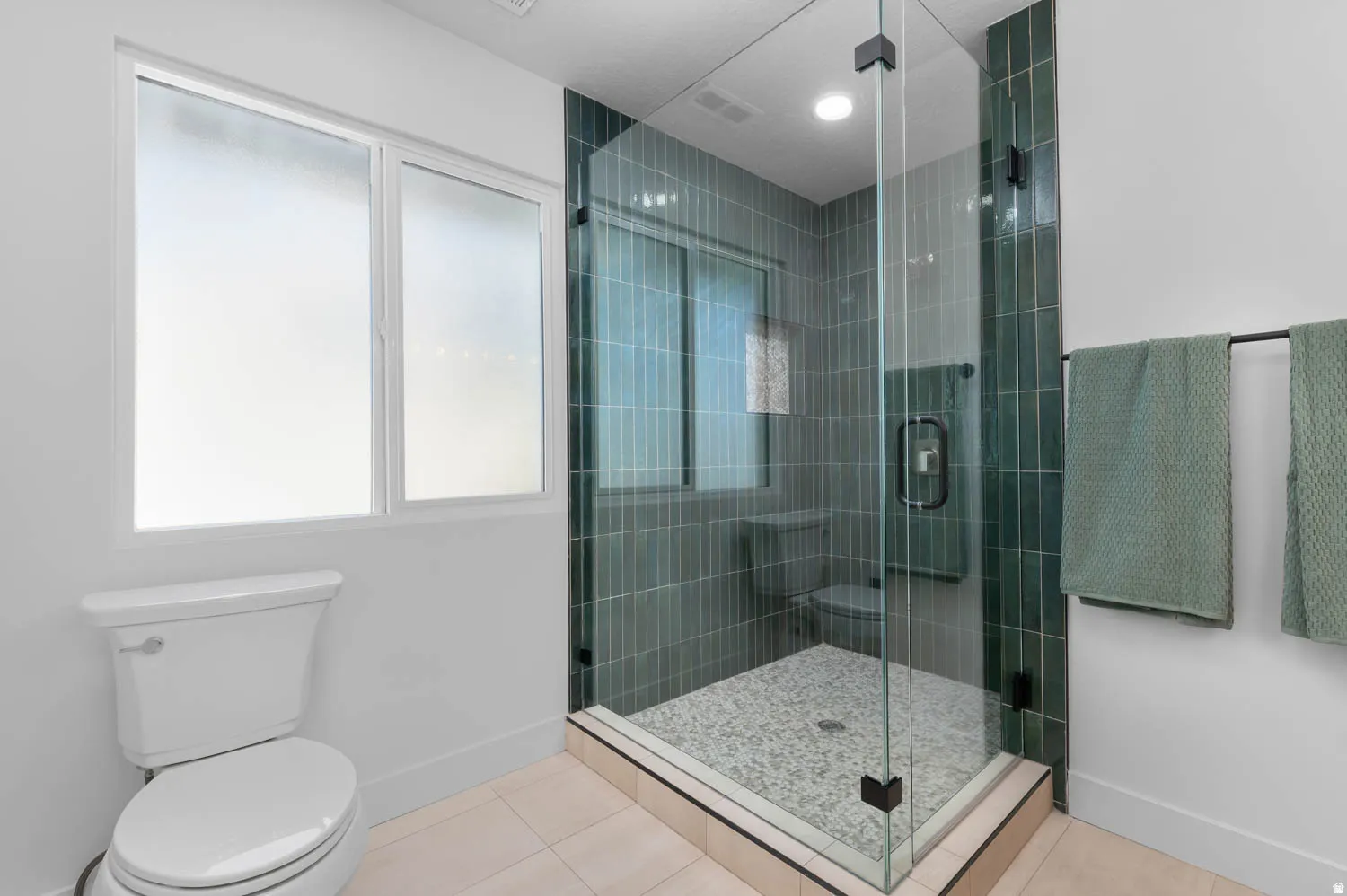 Glass-enclosed shower with vertical teal tile surround and pebble-finish floor