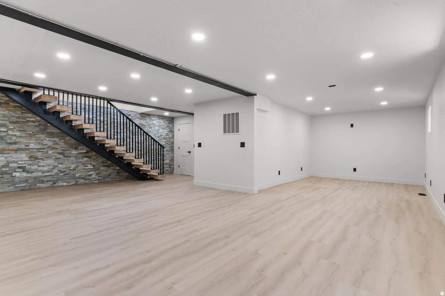 Spacious room featuring light wood-finish flooring, recessed lighting, and white baseboards