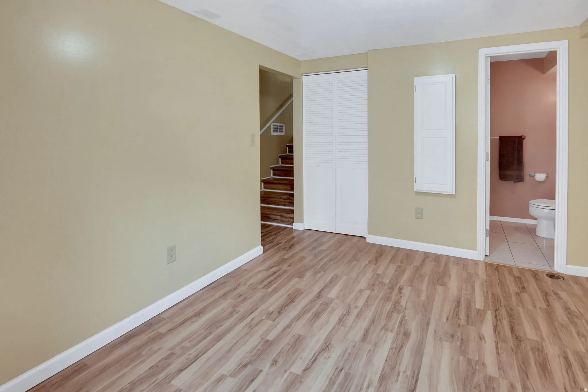 Spacious room featuring wood-finish flooring, light-toned walls, and white baseboards