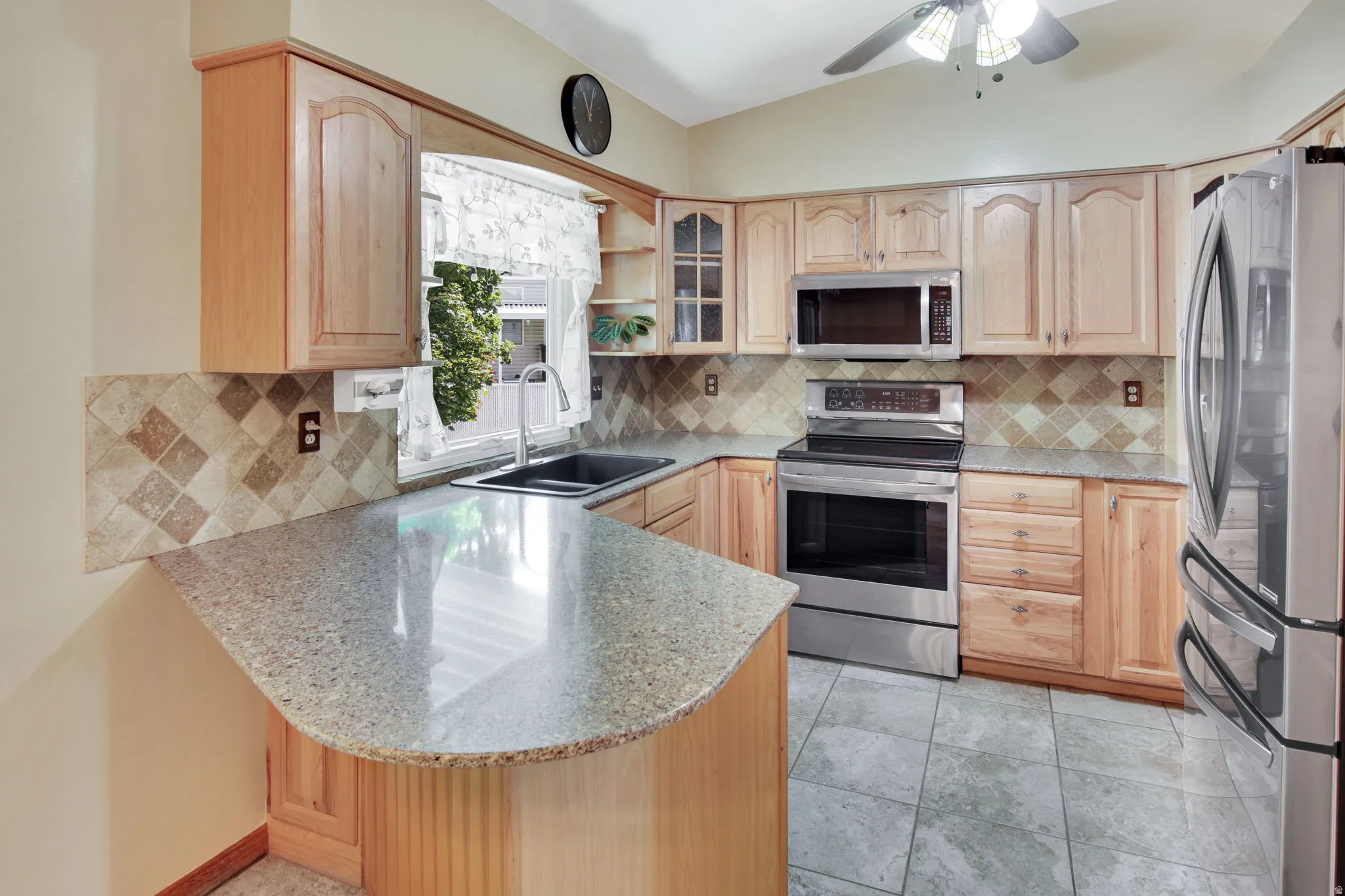 Kitchen featuring light wood cabinetry, a built-in microwave, stainless steel appliances, and a curved peninsula with a stone-finish countertop