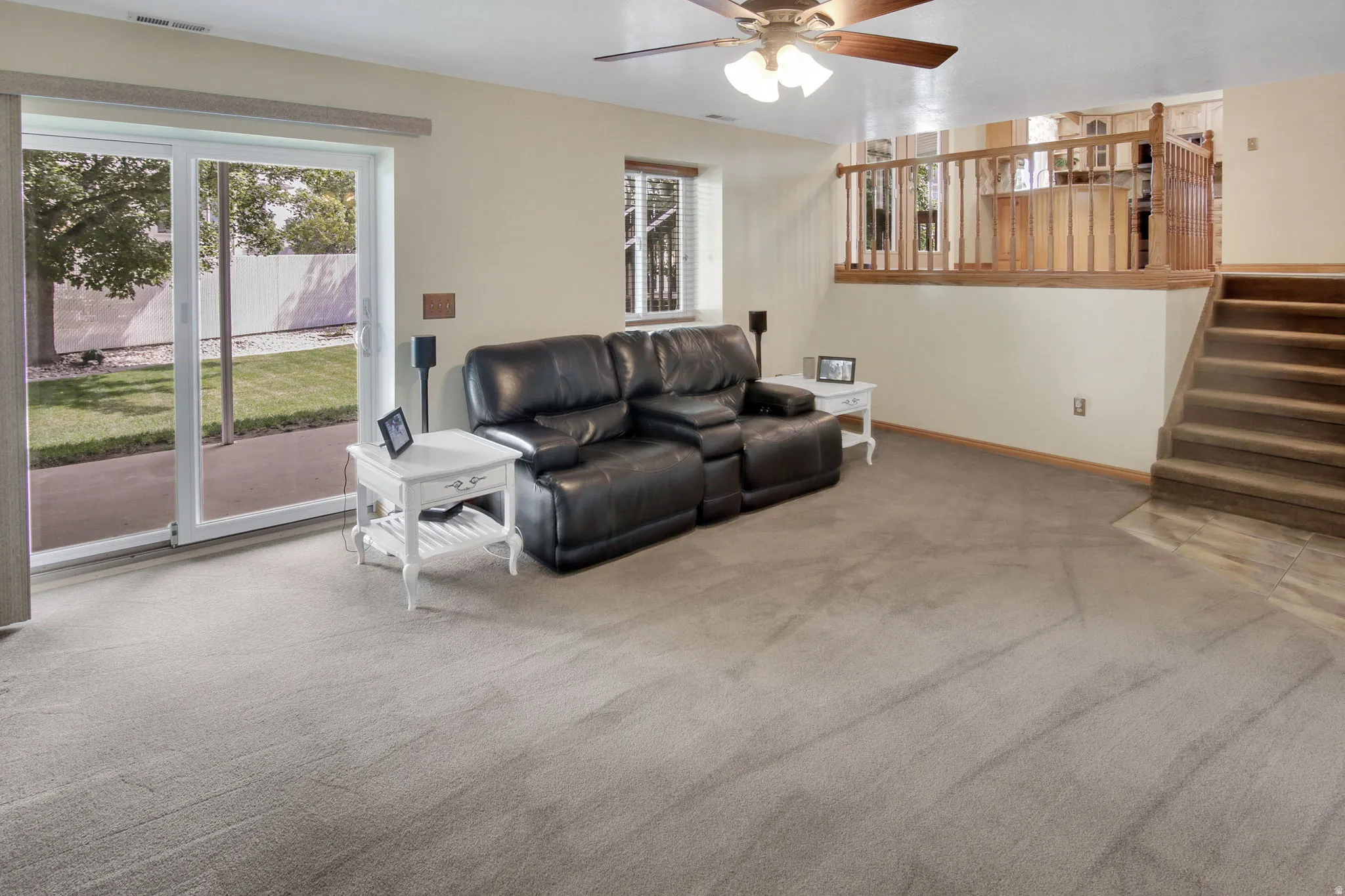 Lower-level living area with neutral carpeting, wood-finish ceiling fan, and sliding glass door
