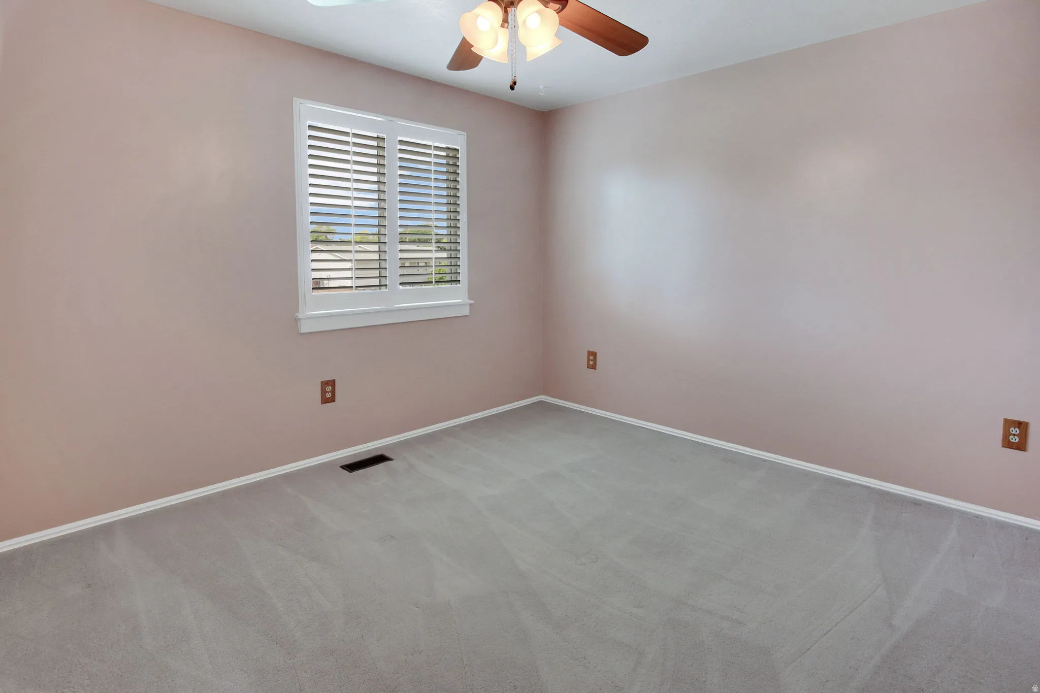 Spacious room featuring light-colored walls, grey carpeting, and a white-framed window with plantation shutters