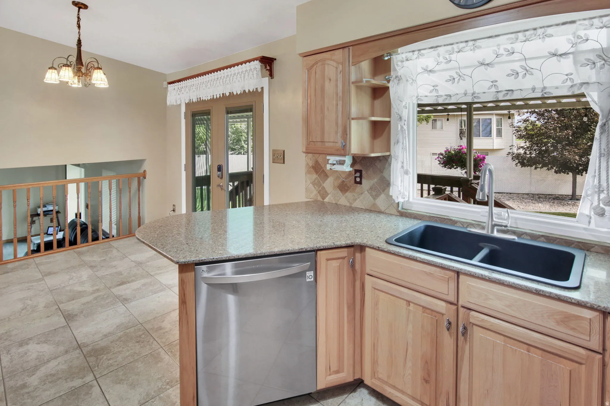 Kitchen featuring granite countertops, a double basin sink with a gooseneck faucet, light wood cabinetry, and a stainless steel dishwasher
