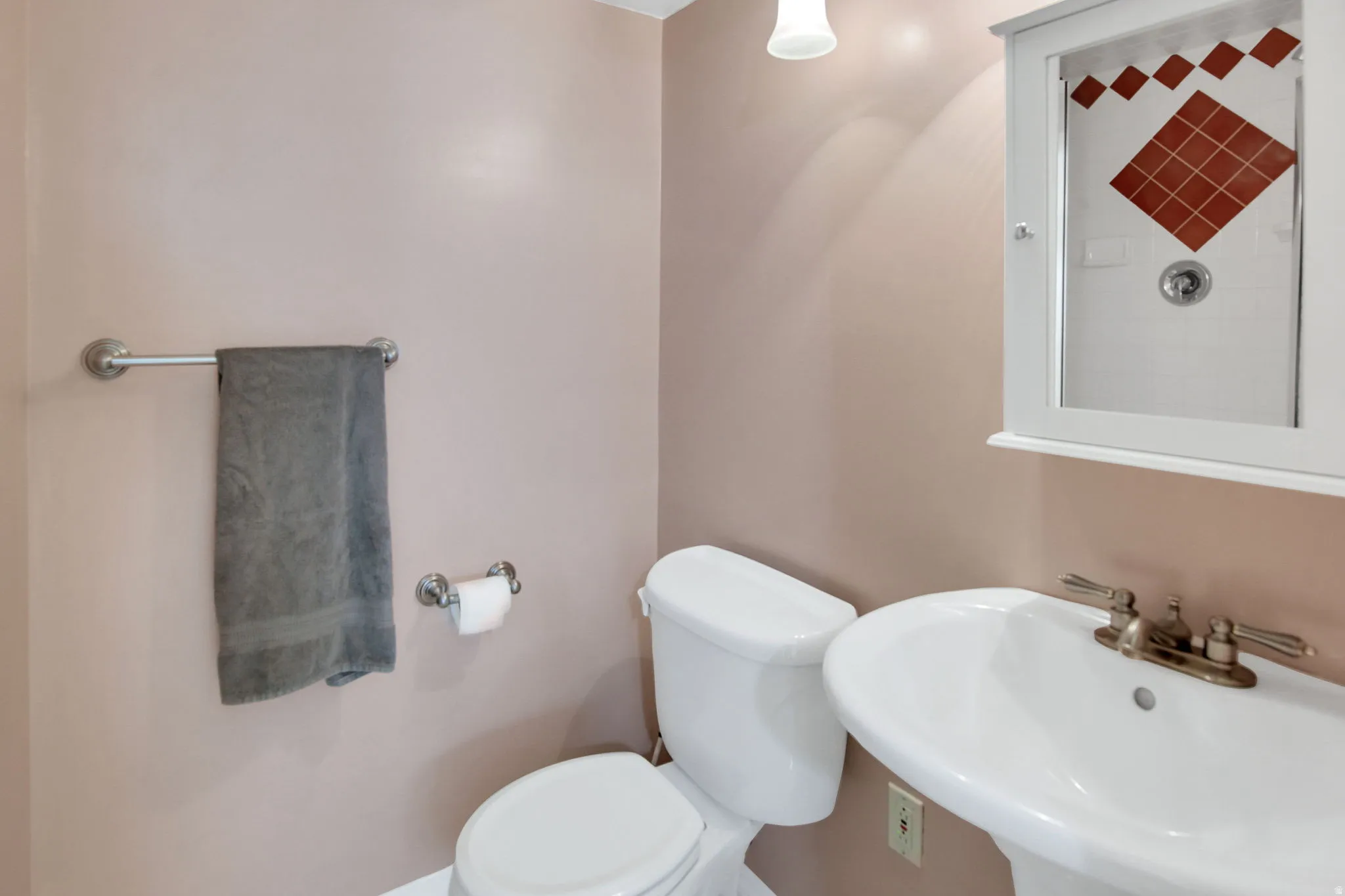 Pedestal sink with brass-finish faucet, white toilet, and a white medicine cabinet with mirrored door