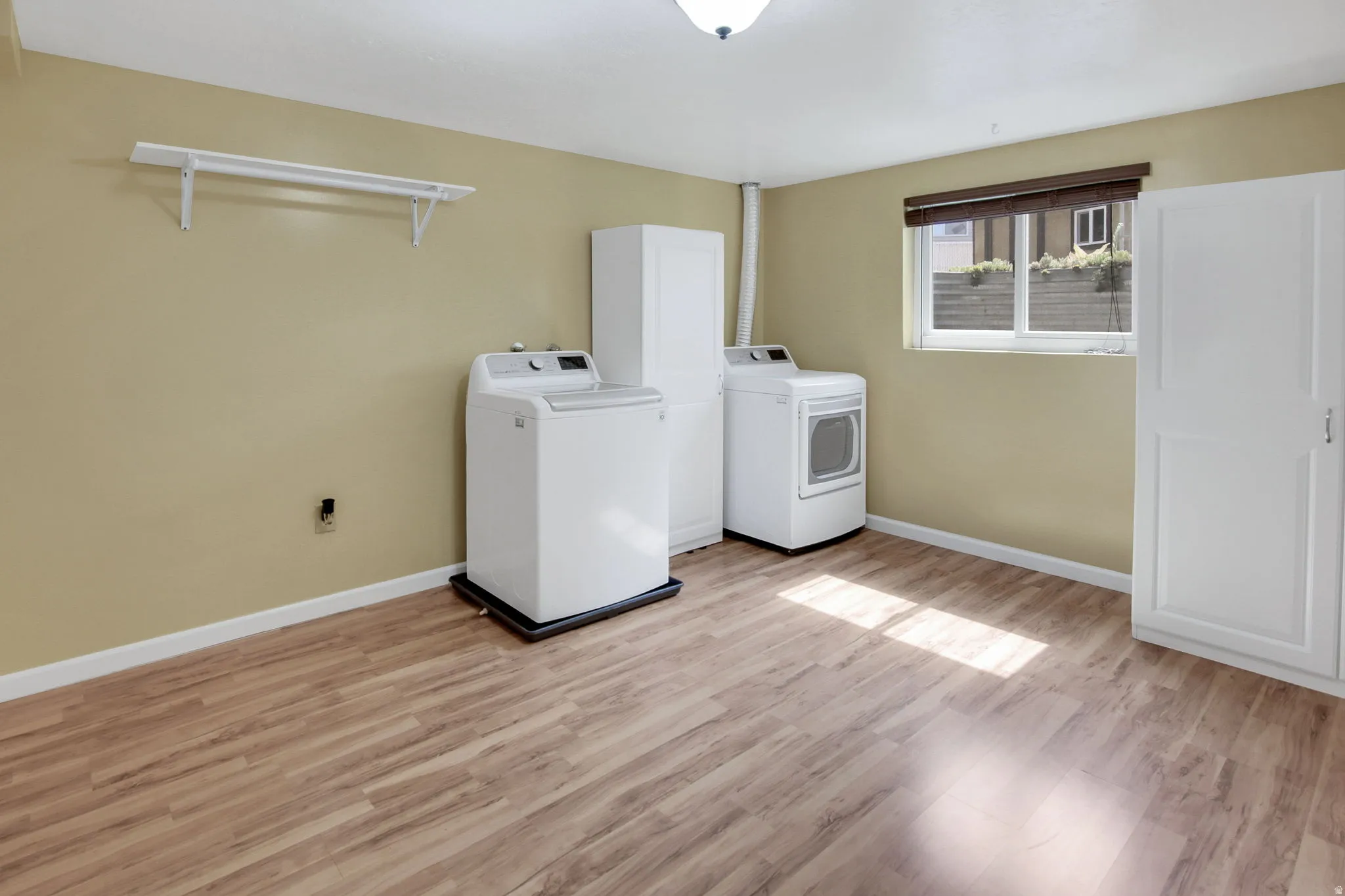 Dedicated laundry area featuring durable wood-finish flooring, a white built-in storage cabinet, and a functional window with privacy blinds
