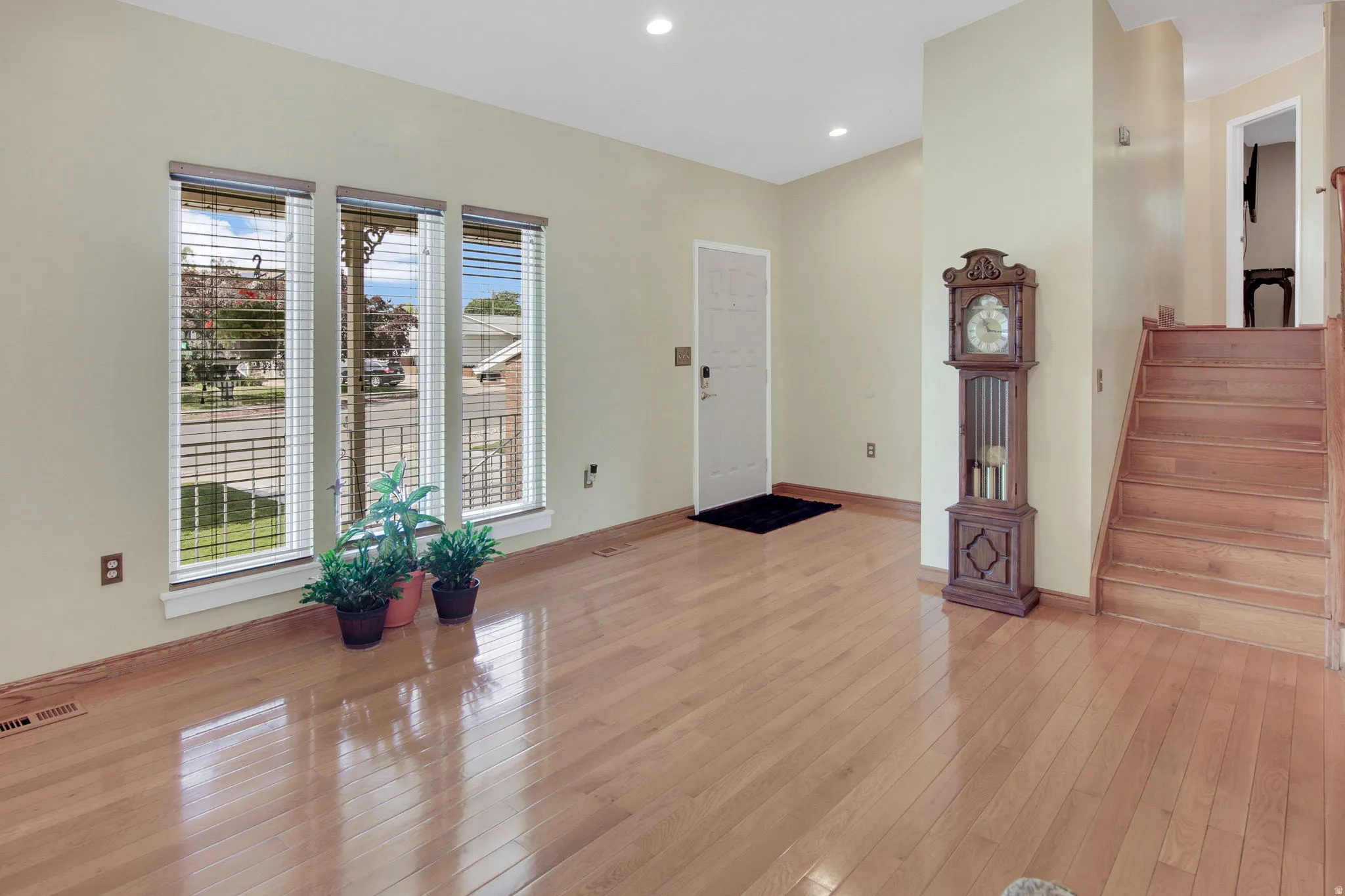 Entryway featuring light wood-finish flooring, a white paneled door, three vertical windows with blinds, and a wood staircase