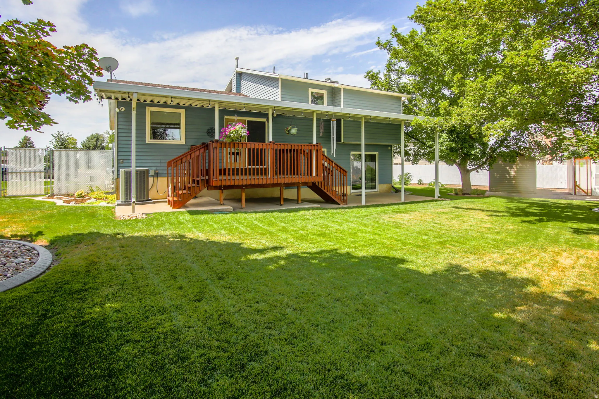Expansive backyard featuring a lush lawn, mature trees, and a raised wood deck with staircase access