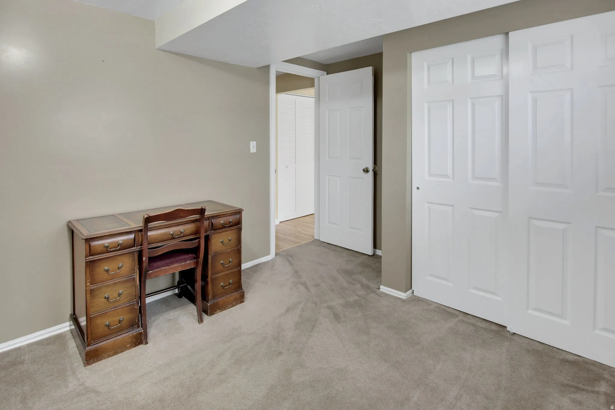 Carpeted room featuring neutral wall tones, white baseboards, and white six-panel bi-fold closet doors