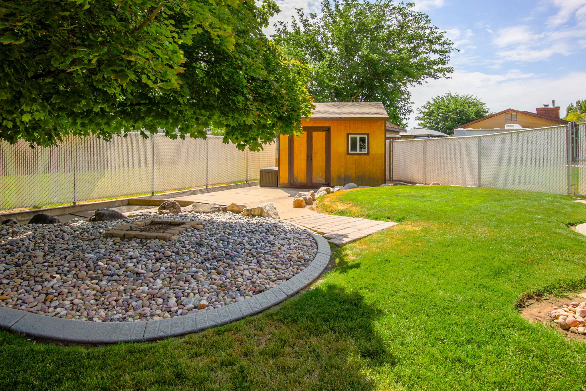 Expansive backyard featuring a manicured lawn, a gravel fire pit area with paver edging, a concrete patio, and a dedicated storage shed