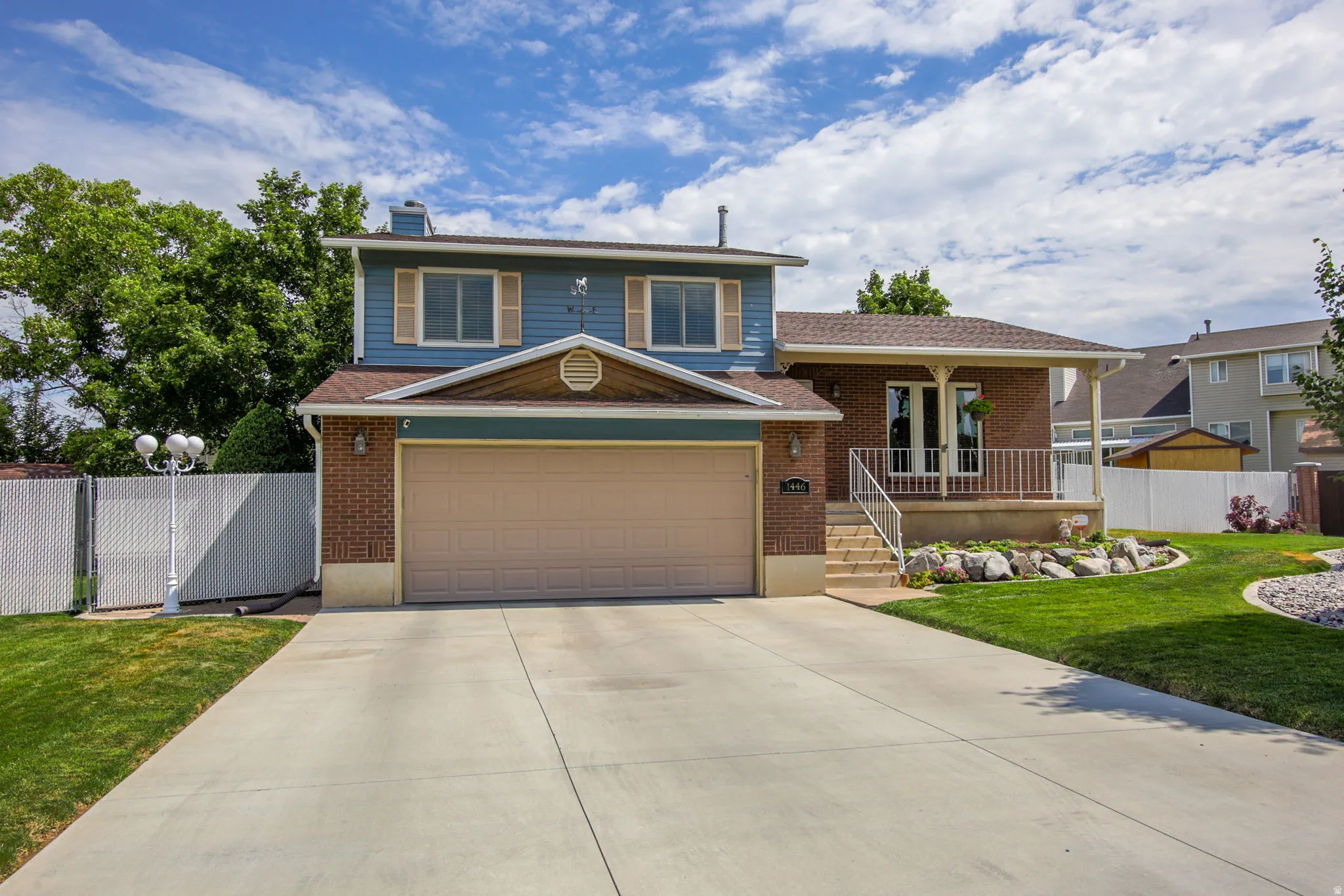 Two-story residence featuring a two-car garage, brick and siding exterior, front porch with white railing, concrete driveway, and manicured lawn with rock landscaping