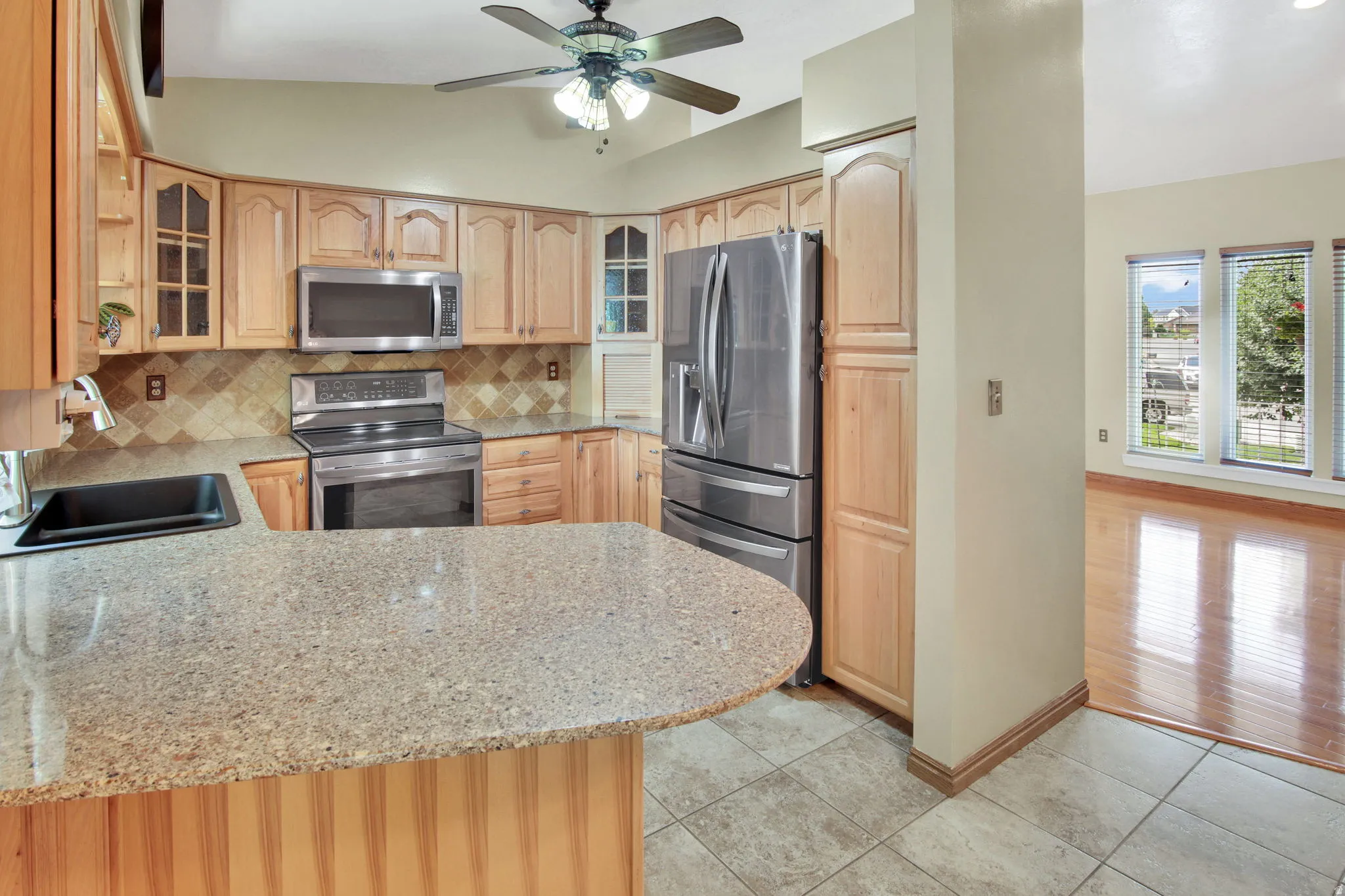 Kitchen featuring light wood cabinetry, stainless steel appliances, a tiled backsplash, an eat-at countertop, and tiled flooring