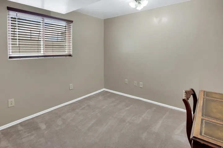 Carpeted room featuring a window with horizontal blinds, neutral wall paint, and white baseboards