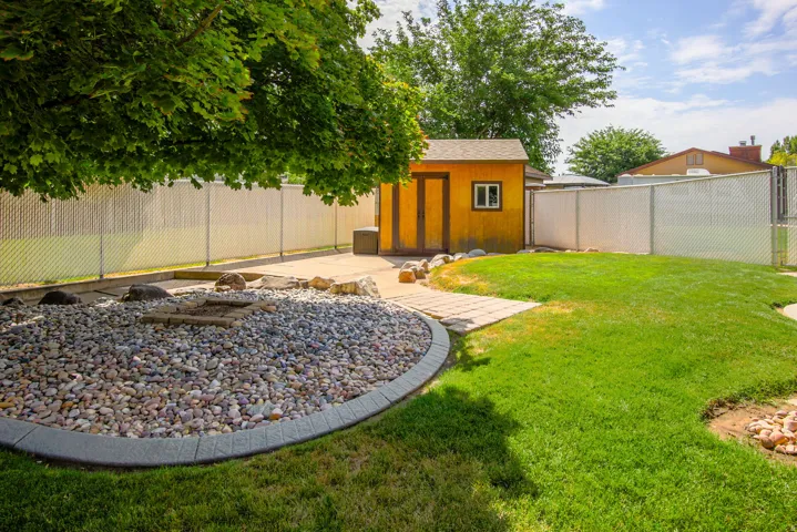 Expansive backyard featuring a manicured lawn, a gravel fire pit area with paver edging, a concrete patio, and a dedicated storage shed