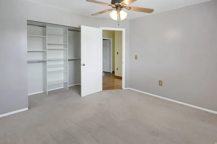 Bedroom featuring carpet flooring, a ceiling fan with light fixture, and a built-in closet system with shelving and hanging rods