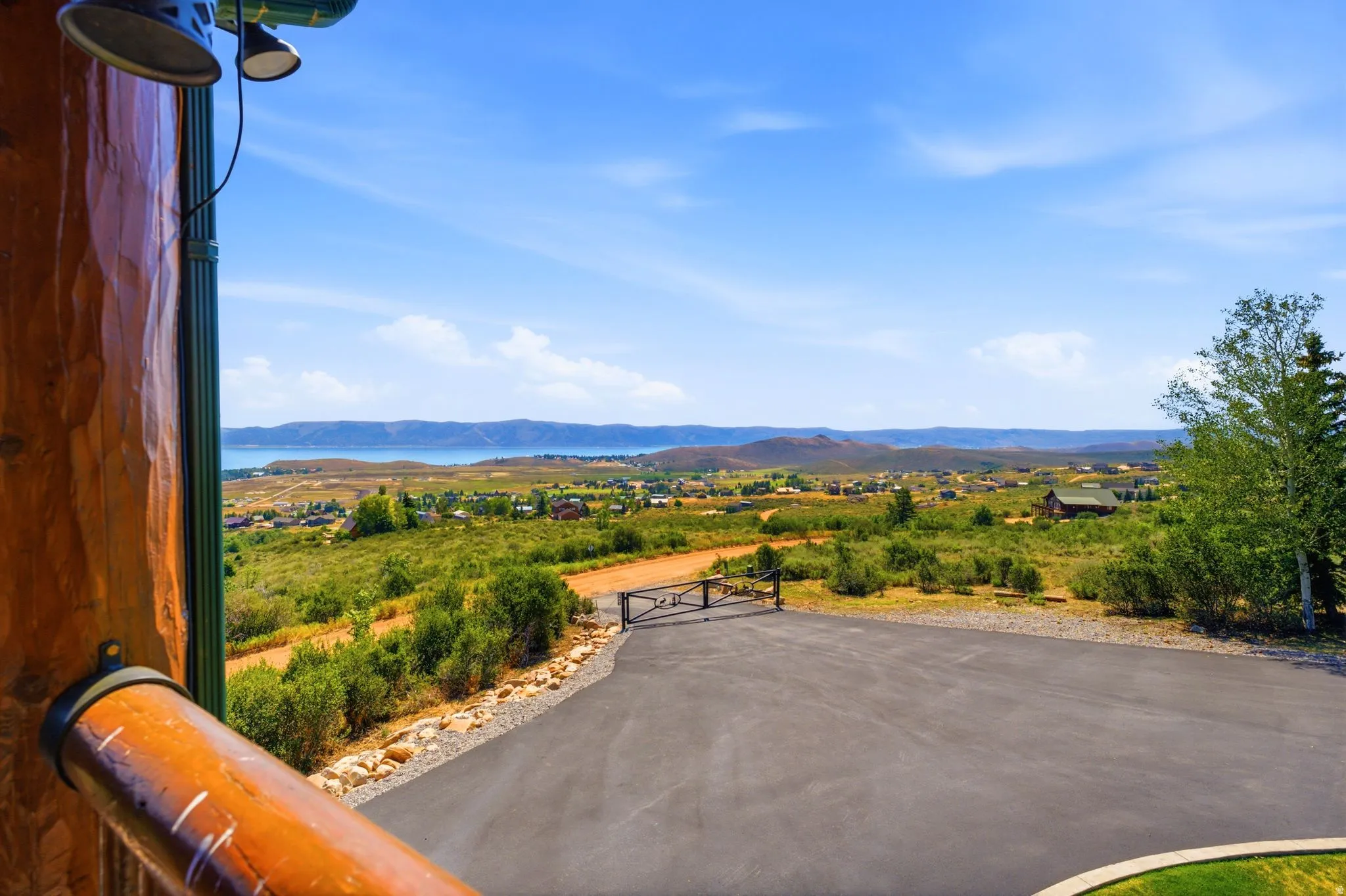 Expansive outdoor setting with a paved driveway, natural landscaping, distant water body, and rolling hills under a clear sky