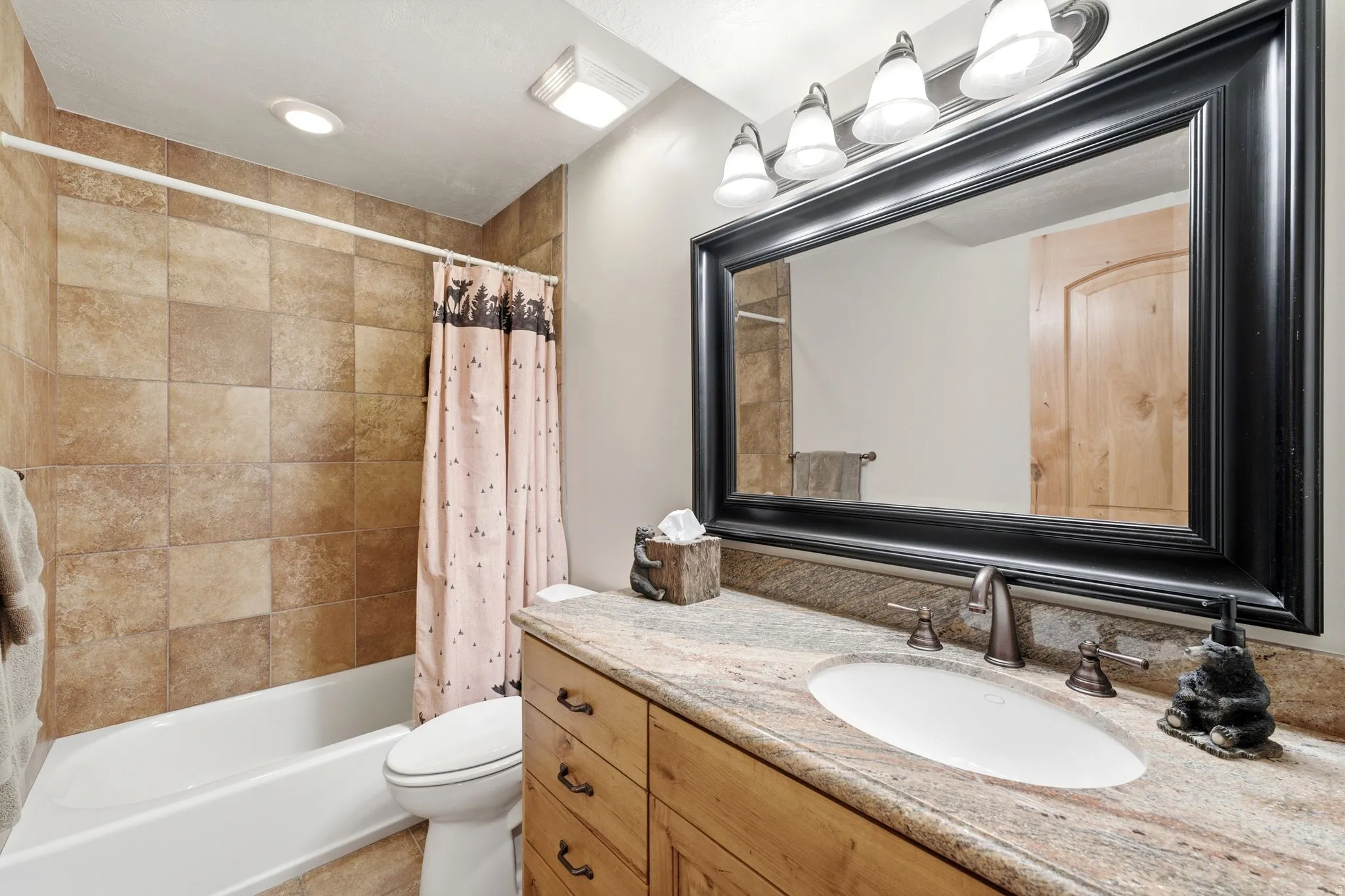 Bathroom featuring a vanity with a light-toned stone countertop, an undermount sink, and a dark-framed mirror