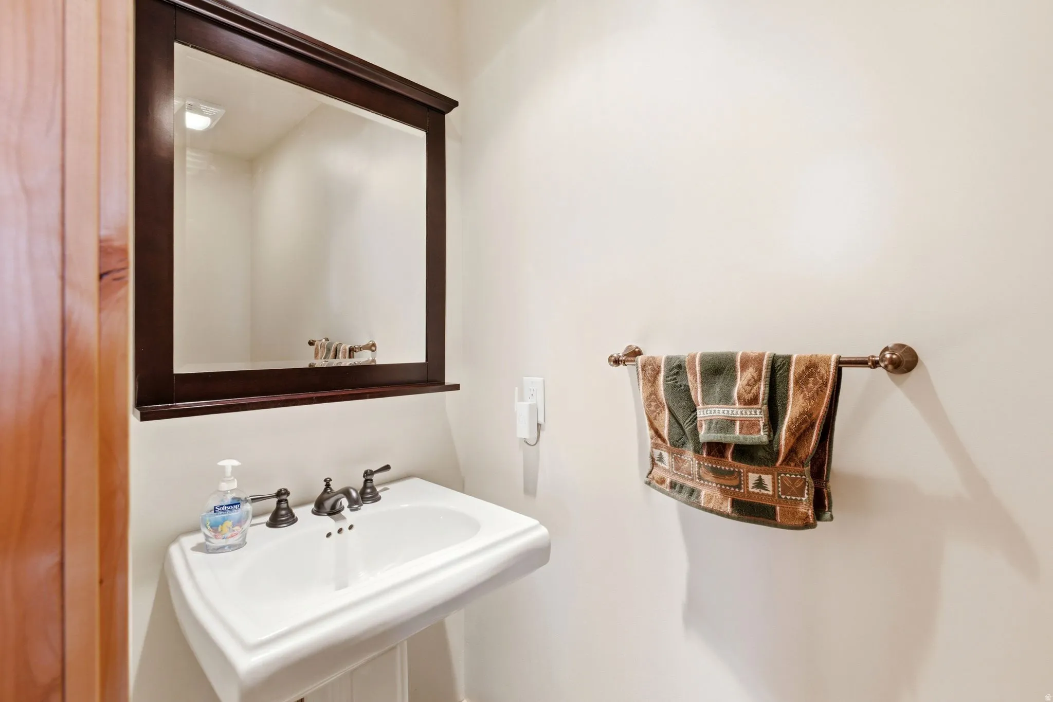 Pedestal sink with dark bronze faucet, framed mirror with integrated shelf, and wall-mounted towel bar