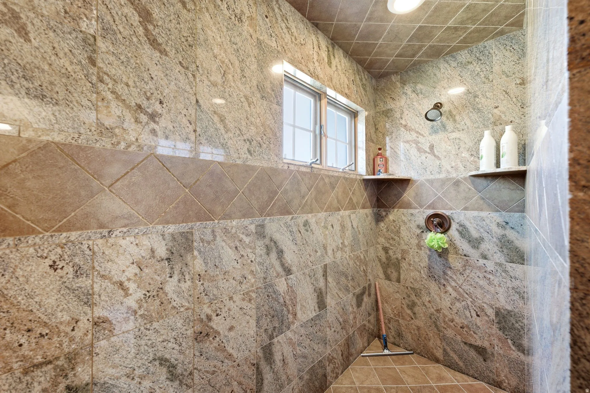 Tiled shower enclosure featuring stone-look wall tiles, a decorative accent band, and recessed ceiling lighting