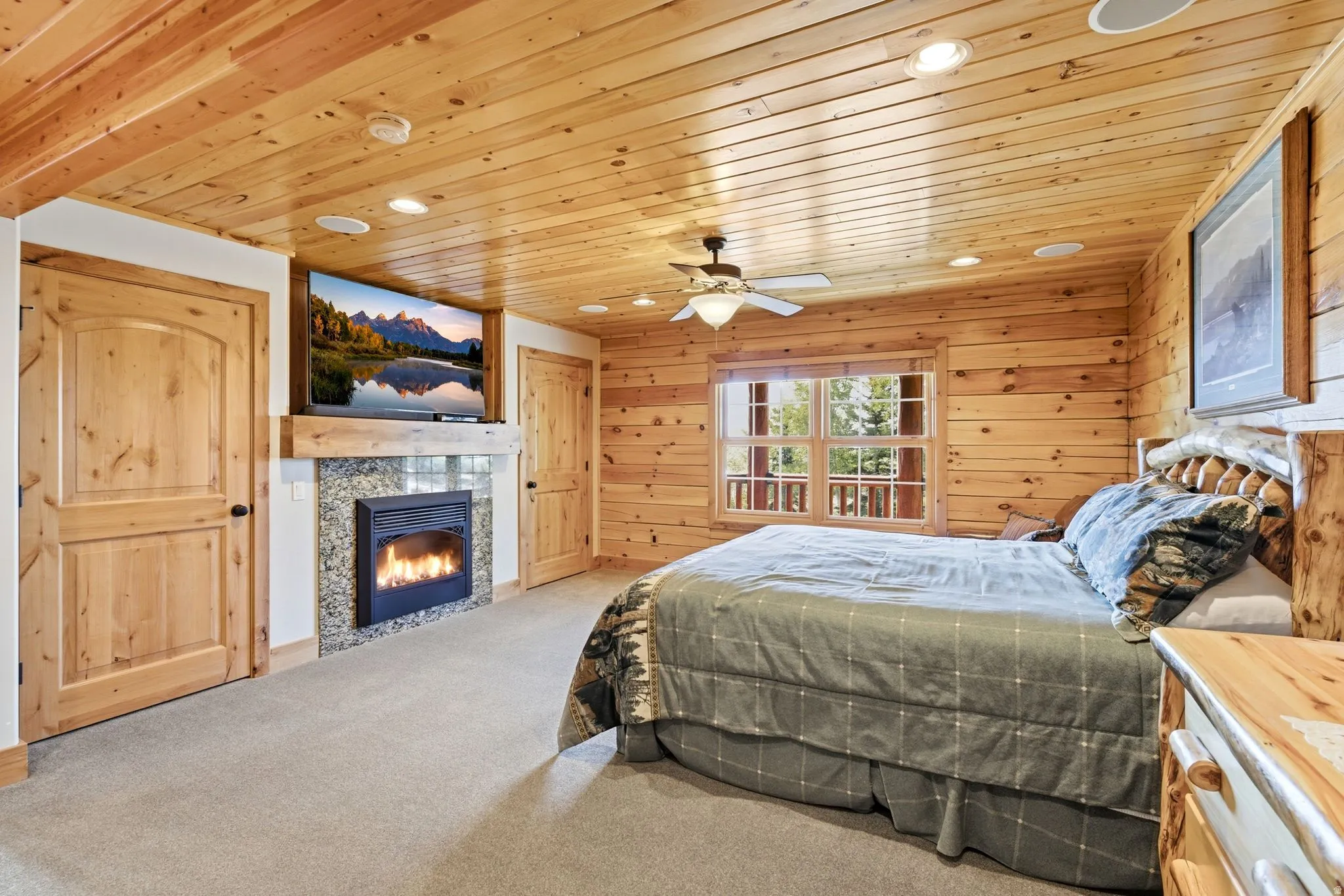 Room featuring wood-plank walls and ceiling, a built-in fireplace with a stone surround, a window with exterior railing visible, two paneled wood doors, and recessed ceiling lighting