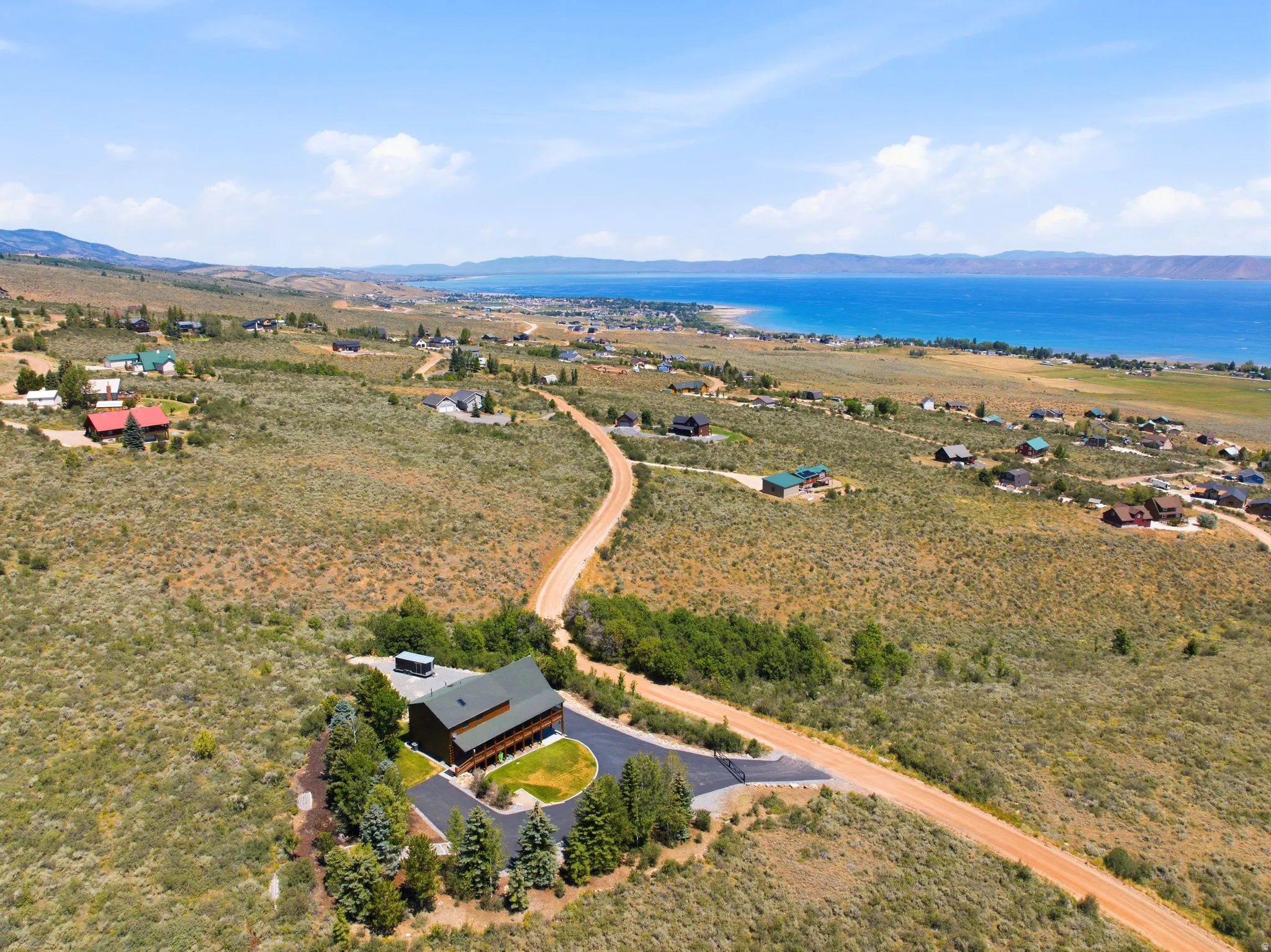 Lakefront property featuring a sloped lot, a paved driveway, mature trees, and a multi-level structure with a balcony