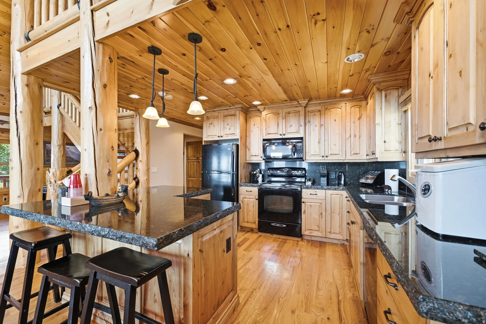 Kitchen featuring knotty wood cabinetry, black appliances, a granite-finish countertop with a live edge, and a wood-plank ceiling