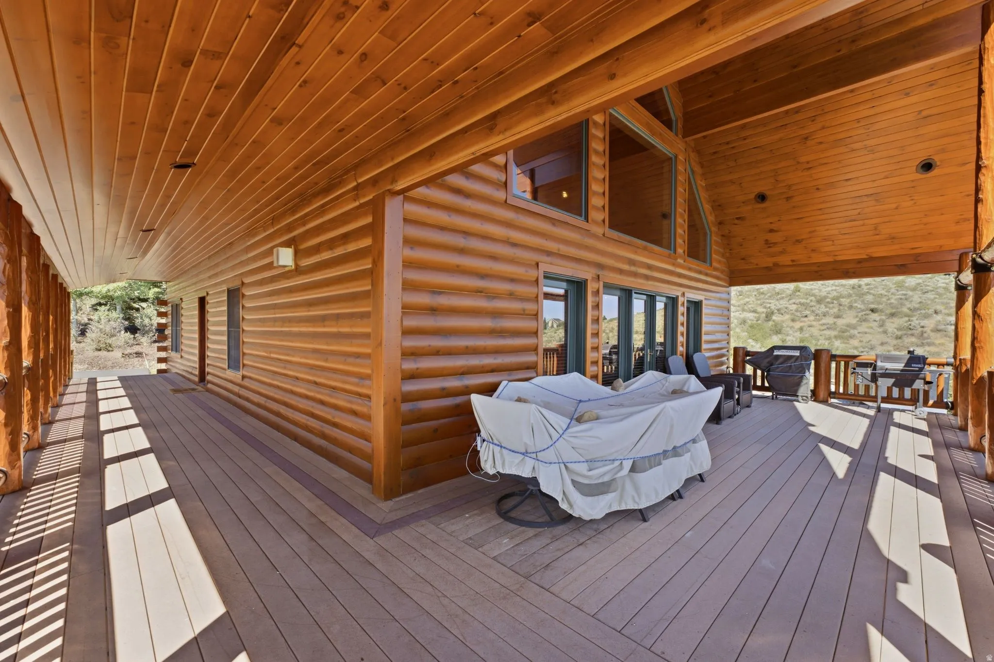 Expansive wrap-around deck featuring composite flooring, log construction, and a covered ceiling