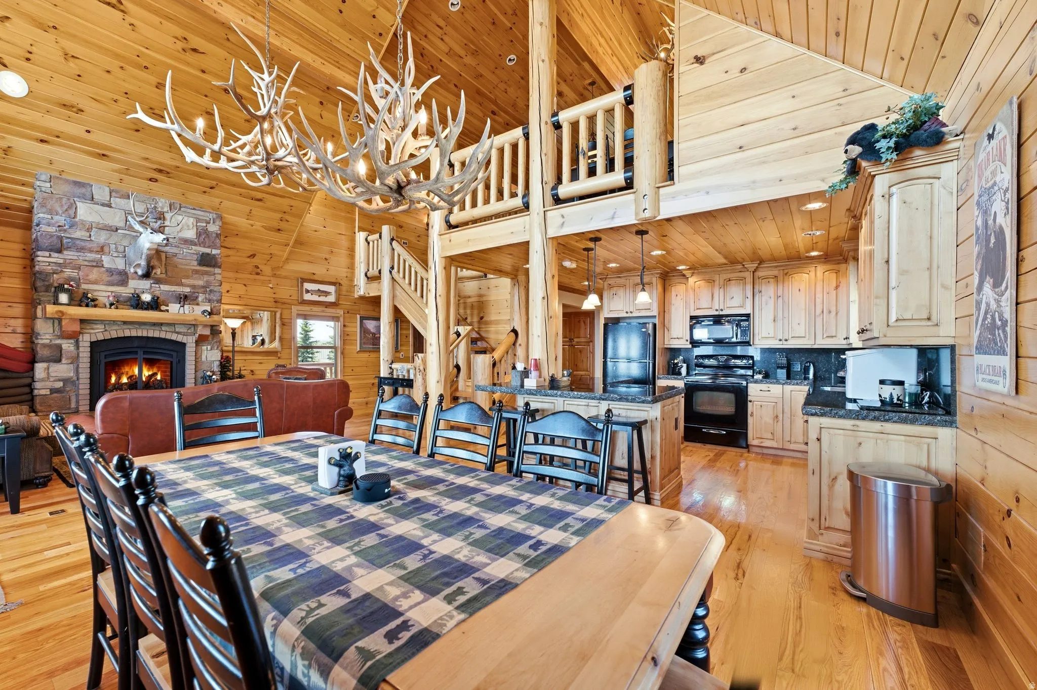 Open-concept living area featuring a stone fireplace, wood-finish flooring, and exposed wood plank walls and ceilings