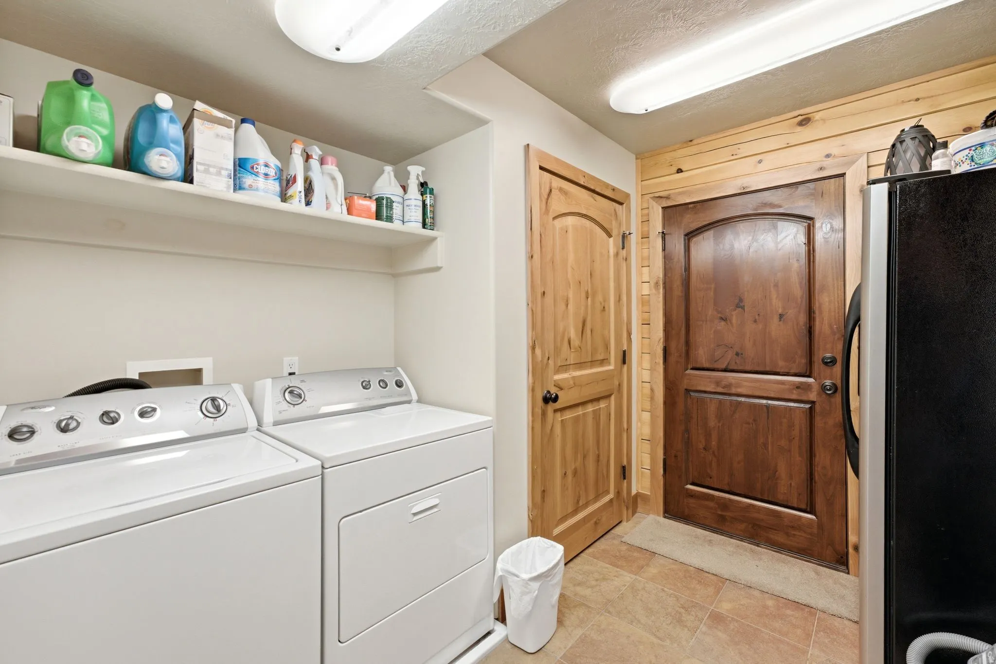 Dedicated laundry area featuring a washer and dryer, an overhead storage shelf, recessed lighting, wood-finish flooring, and two wood-paneled doors