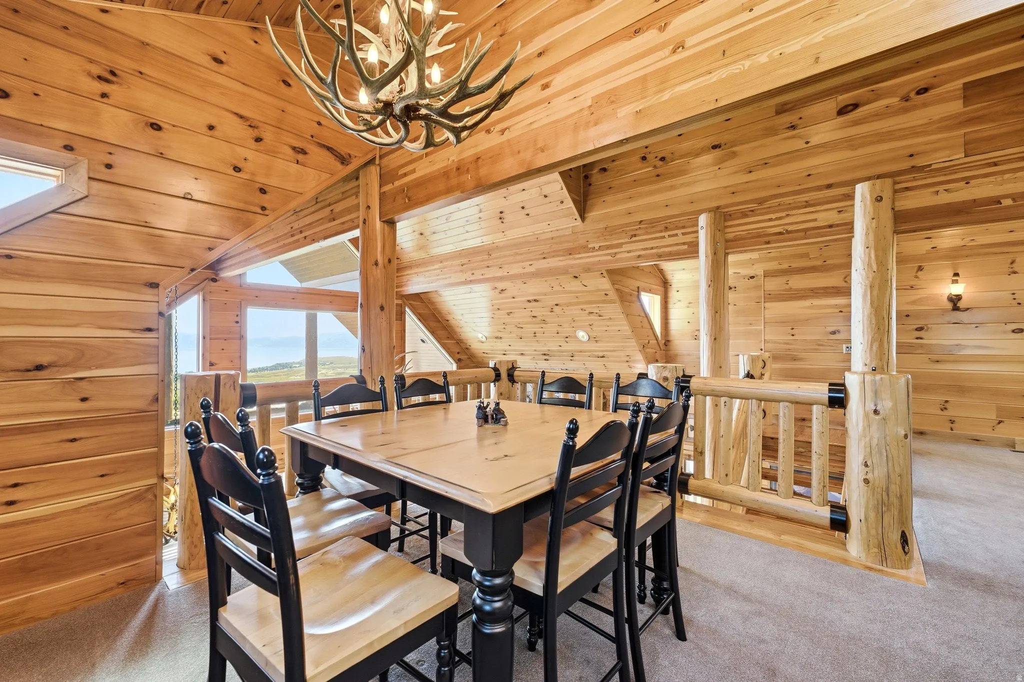 Spacious dining area featuring natural wood paneling, a distinctive antler chandelier, and log-style railings