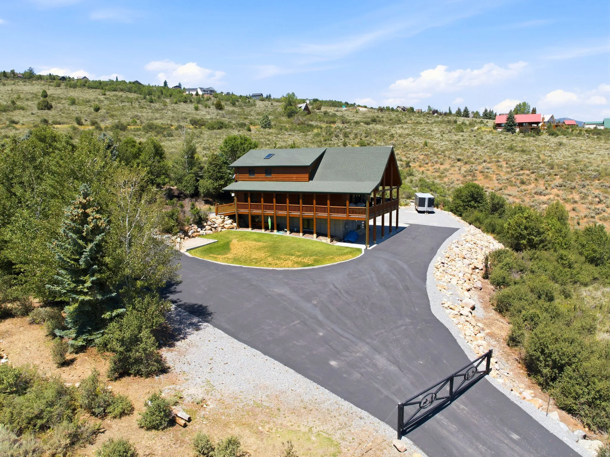 Log-style residence with a dark green roof, featuring an expansive wrap-around porch and a lower-level patio