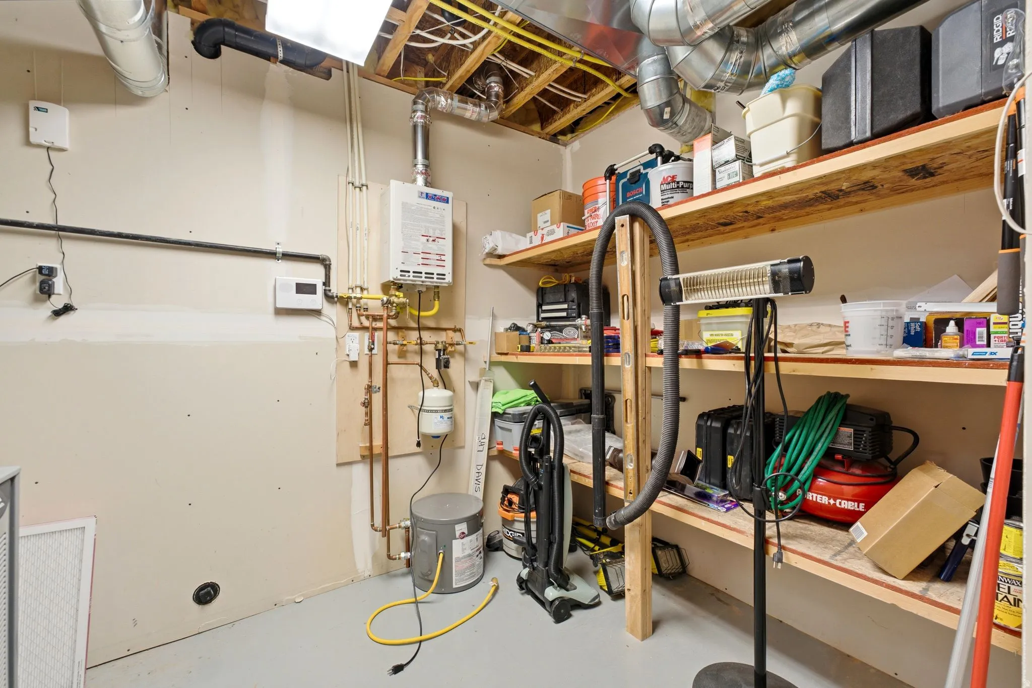 Utility room featuring a tankless water heater, exposed ductwork, and built-in wood shelving for storage