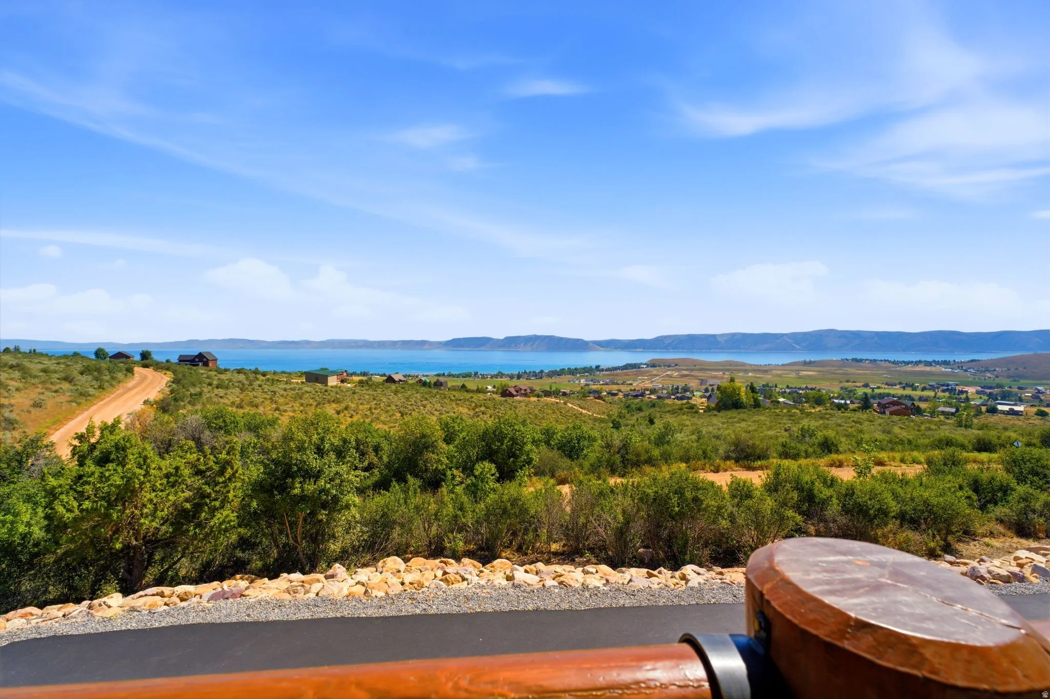 Expansive landscape featuring a large body of water, distant hills, and varied vegetation under a clear sky
