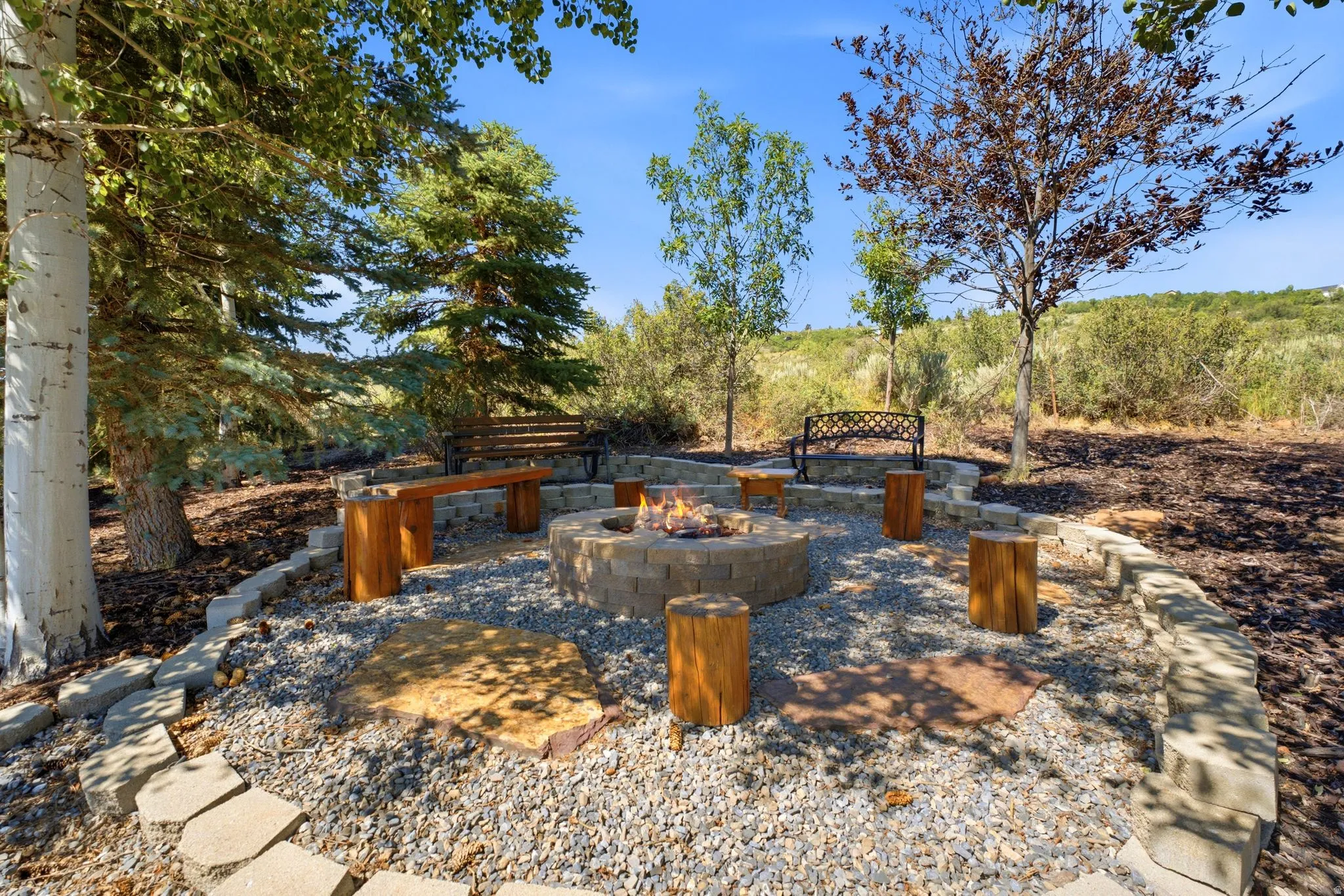 Outdoor fire pit area with an integrated seating wall, gravel surfacing, and natural tree stump seating