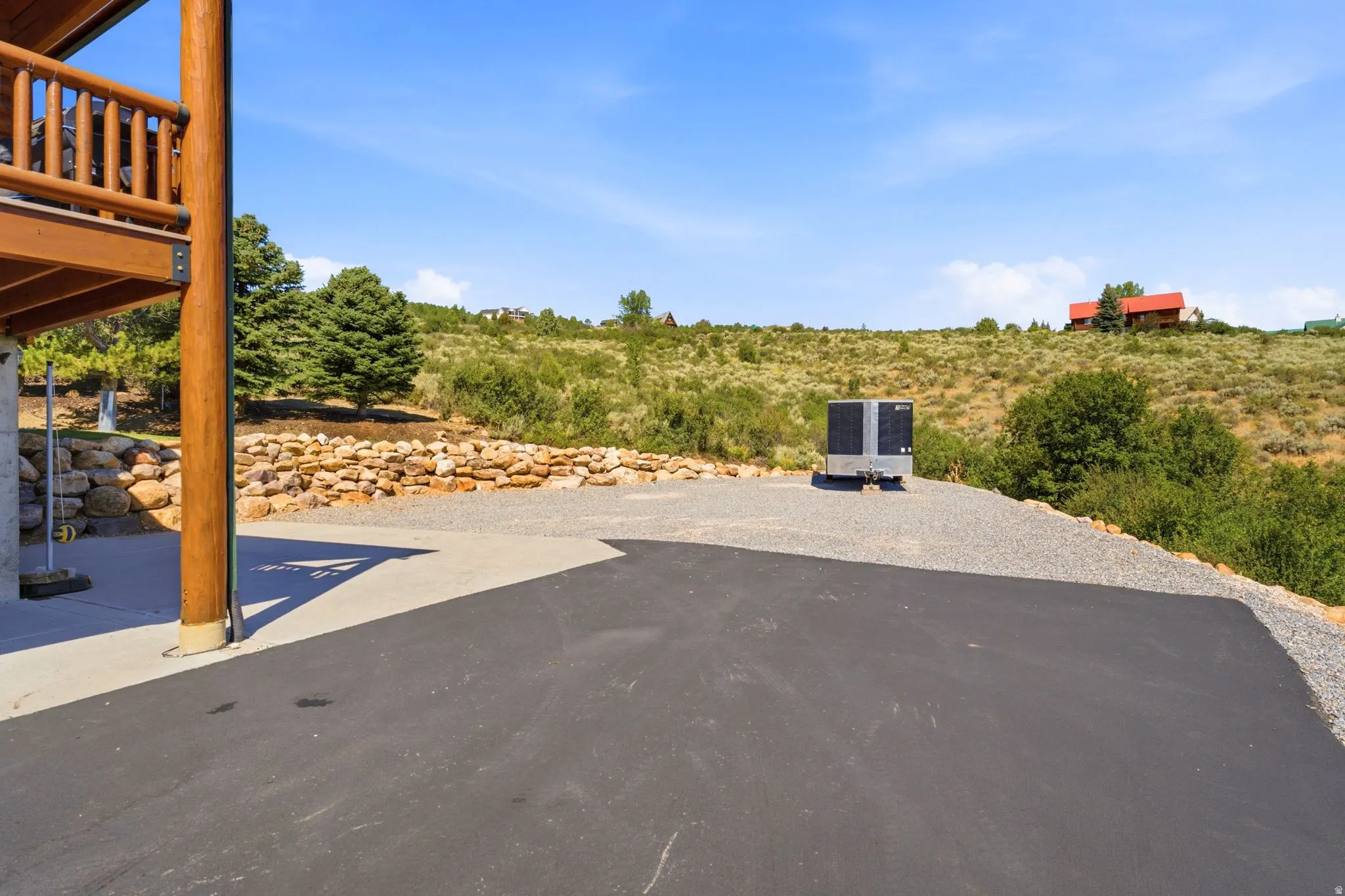 Expansive paved and gravel driveway with a substantial wood support beam and upper deck framing