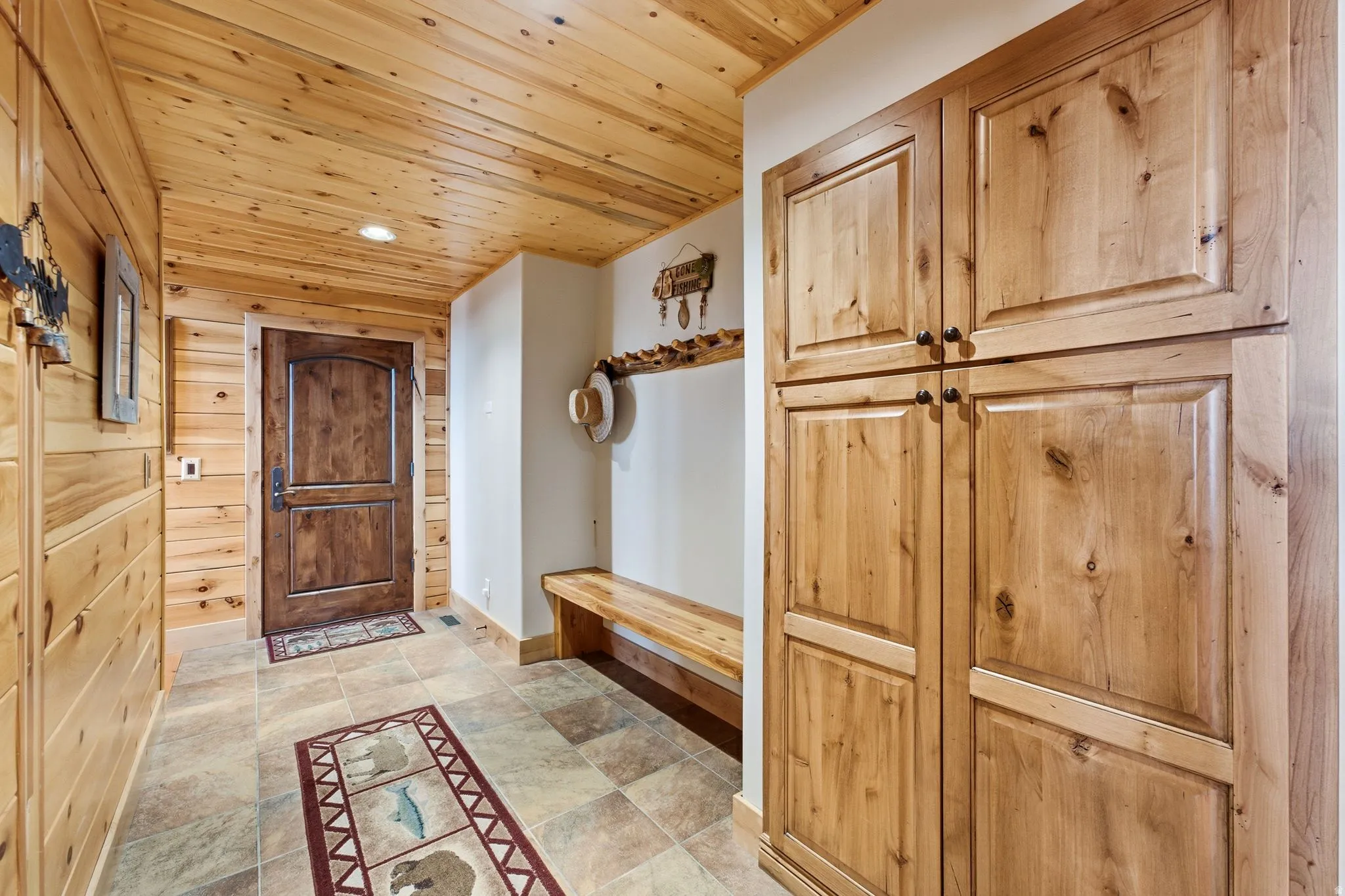 Entryway featuring wood-paneled walls and ceiling, a built-in wood bench, and integrated wood cabinetry