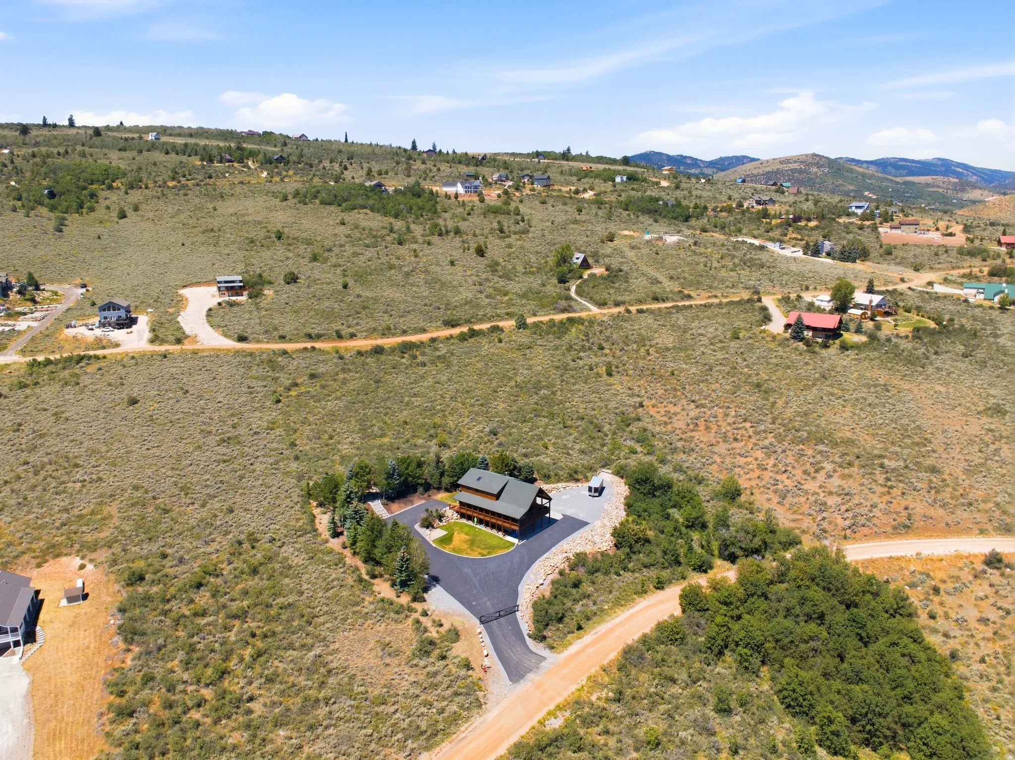 Expansive property featuring a two-story residence with a dark roof, a paved driveway, and surrounding mature trees