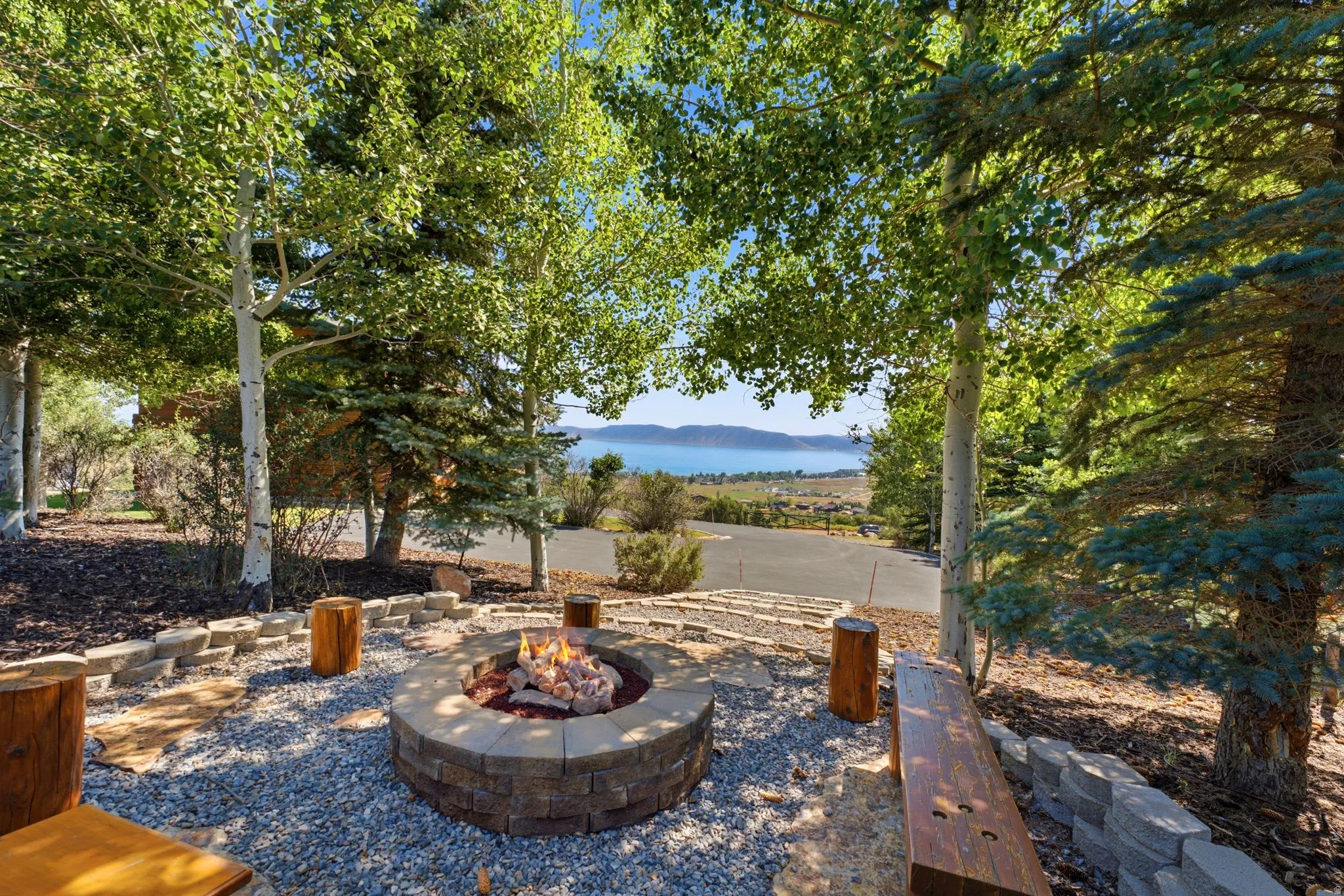 Stone fire pit surrounded by gravel, featuring several wood benches and tree stump seating