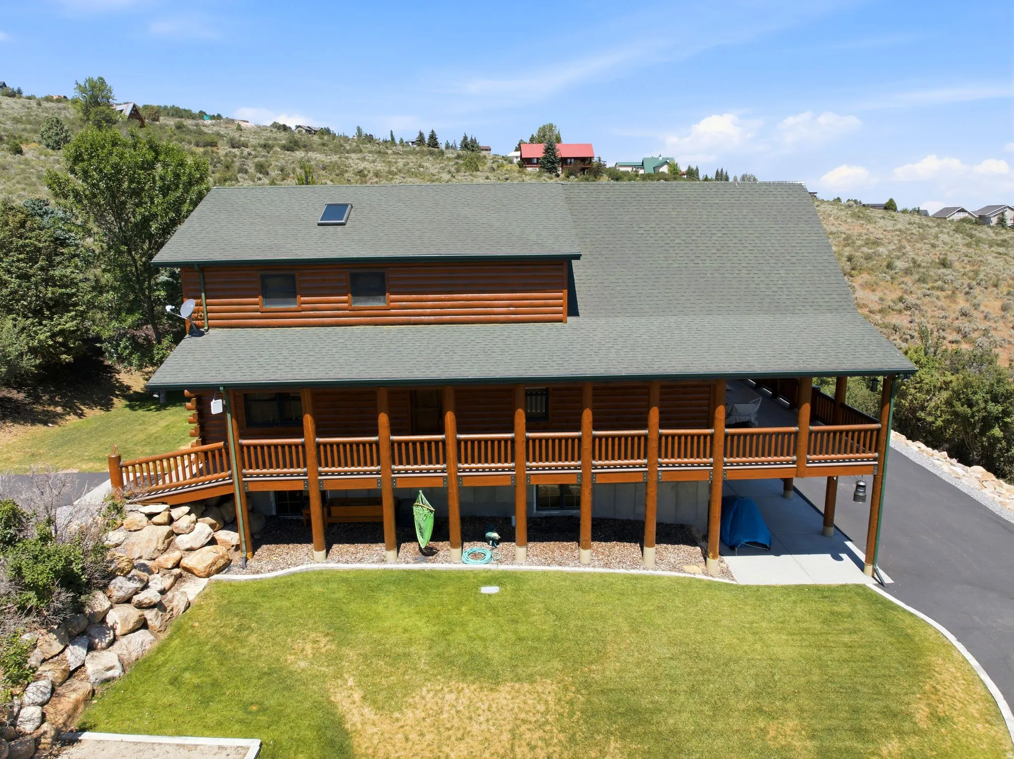 Log cabin exterior featuring a covered porch, a lower-level patio, a skylight, a verdant lawn, and a paved driveway