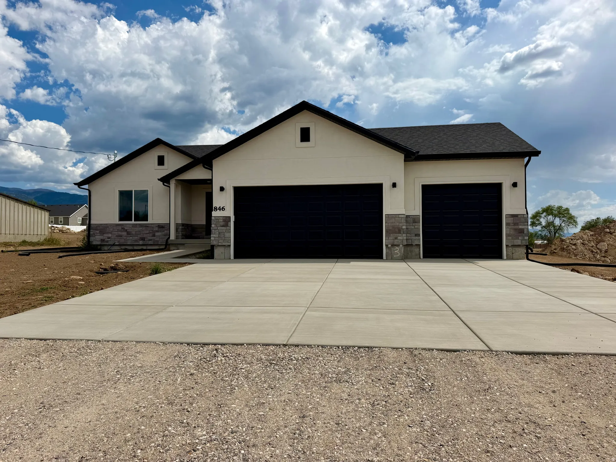 New ranch-style home featuring a cream stucco facade and dark gray stone accents